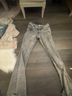 Grå bootcut jeans låg midja - Säljer ett par grå bootcut jeans med låg midja och klassisk femficksdesign. Jeansen har en tvättad look och är tillverkade i jeansmaterial. Passformen är loose upptill och blir vidare nedtill. Perfekta om du gillar retrovibbar och vill ha något som sticker ut. Köpare betalar frakt! 