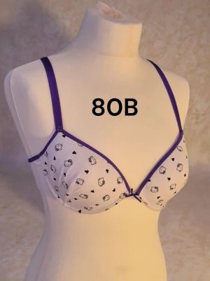 Ny Hello Kitty behå 80B - Vit äkta Hello Kitty bh med lila detaljer med orginal lappen på. Tunna kupor. 95% bomull. 5% elastan. Varan är oanvänd och kommer från ett konkurslager från 2000-talet. I många fall är prislappen kvar (se bild). Har fler annonser och bra bundlerabatt vid köp av flera.