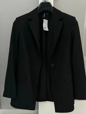 Svart kavaj från H&M Divided XS - Svart kavaj med lappar kvar, från H&M Divided i storlek XS. Klassisk modell med två knappar framtill, krage och fickdetaljer. Perfekt för en clean och stilren look. 