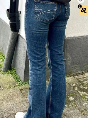Blå bootcut jeans från junkyard - Snygga blå bootcut jeans från junkyard med klassisk femficksdesign och ljus tvätt på låren. Jeansen har låg midja och är tillverkade i slitstarkt denim med stretch för extra komfort. Perfekt passform och coola detaljer på bakfickorna lite slitna längst ner.