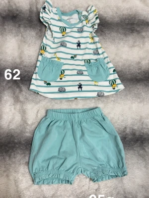 Polarn o pyret sommar set - Söt babyklänning med ljusblå och vita ränder, dekorerad med djurmotiv som elefanter och giraffer samt luftballonger. Puffärmar och två ljusblå fickor framtill. Tillhörande ljusblå shorts med resår i midja och benslut. Perfekt för varma dagar!🌸 Använd en gång. Storlek 62