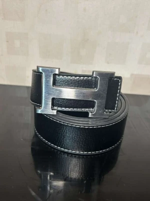 En svart bälte med ett silvrigt h spänne  - En svart snygg bälte stilren aldrig använd skick 10/10