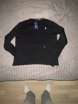 Svart kabelstickad tröja Polo Ralph Lauren helt ny - Svart kabelstickad tröja från Polo Ralph Lauren i storlek M. Tröjan har rund hals, långärmade ribbade muddar och den klassiska broderade loggan på bröstet. Materialet är mjukt och stickat, perfekt för kyliga dagar. Säljer den då den ej passade mig. Den är i perfekt skick. Hör av er om frågor.
