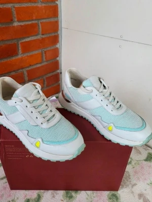 Michael Kors mintgröna sneakers - Fräscha sneakers från Michael Kors i mintgrönt och vitt med meshpaneler och detaljer i skinn. Snygga silverdetaljer på hälen och coola gula accenter framtill. Skorna har snörning och platt sula, perfekt för en trendig look.