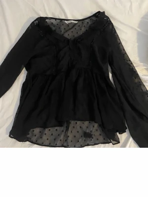 Svart prickig blus från Stradivarius - Säljer en svart blus från Stradivarius i storlek S. Blusen är transparent med prickigt mönster, har volangdetaljer och v-ringning. Långärmad och lätt material som ger en luftig känsla. Perfekt för dig som gillar romantiska detaljer och stilren look.