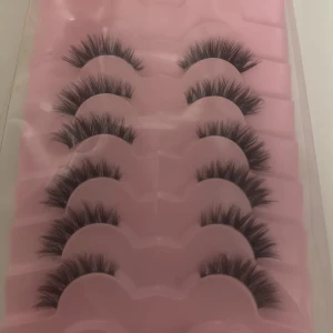 Falska ögonfransar i 5-pack - Säljer ett set med fem par fylliga, svarta lösögonfransar i en rosa plastförpackning. Fransarna har en dramatisk volym och fluffig form, perfekta för att ge ögonen extra intensitet. Passar till dig som vill ha en bold look.