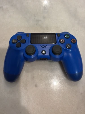 Sony DualShock 4 Wireless Controller (Blå) - Snygg blå Sony DualShock 4 trådlös handkontroll till PlayStation 4. Kontrollen är i fint skick med minimalt slitage, alla knappar och styrspakar ser hela ut. Perfekt för gaming eller som extra kontroll till din PS4. Finns ingen stick-drift på kontrollen. Har haft den i 2 år men knappt använt den på grund av att jag har en playstation 5 med 2 handkontroller.