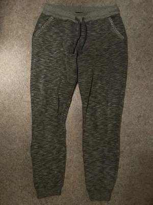 Grå mjukisbyxor från Rich & Royal - Gråmelerade mjukisbyxor från det tyska lyxmärket Rich & Royal. Snörning i midjan och ribbade muddar vid bensluten. Fickorna är dekorerade med guldglittriga diamant detaljer som ger en extra touch. Perfekta för chill dagar eller när du vill vara bekväm men ändå snygg. Nypris på liknande mjukisbyxor på deras hemsida ligger på 1200-1500kr