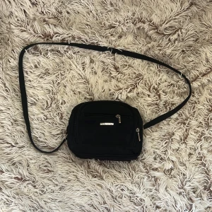 Svart axelväska från Valencina - Praktisk svart axelväska från Valentina med flera fack och dragkedjor. Väskan har en justerbar rem. Perfekt för dig som vill ha ordning på dina grejer och gillar enkel, stilren design. Den har 5 st fak.