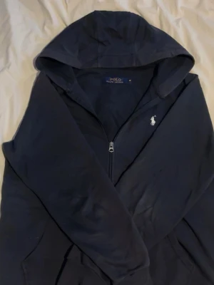 Blå Ralph Lauren Zip Hoodie - Blå Ralph Lauren Zip Hoodie som säljs pga att den inte används tillräckligt. Tröjan är köpt här på plick och är i bra skick! Det är bra kvalité och den är väldigt snygg och skön😁 tröjan är använd 10-15 gånger. Hör gärna av er i DM om ni har några funderingar!