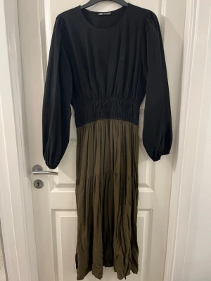 Svart och olivgrön långklänning Zara - Säljer en snygg långklänning från Zara i svart och olivgrönt. Klänningen har rund hals, långa puffärmar och markerad midja med rynk. Kjoldelen är plisserad och ger en cool flowy look. Perfekt för dig som gillar stilrena färger och bekväm passform.
