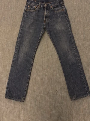 Levi's 501 jeans mörkblå W29 L32 - Klassiska Levi's 501 jeans i mörkblå tvätt med raka ben och fem fickor. Jeansen har knappgylf och den ikoniska läderpatchen bak i midjan. Perfekt passform och tidlös stil, tillverkade i slitstarkt bomullsjeansmaterial.