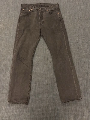 Levi's 501 grå jeans W30 L30 - Säljer ett par klassiska Levi's 501 jeans i grått. Modellen har rak passform, fem fickor och knappgylf. Jeansen är tillverkade i slitstark bomull och har den ikoniska läderpatchen bak i midjan. Perfekt för dig som gillar tidlös stil.