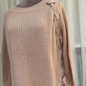 Rosa stickad tröja med snörning - Säljer en rosa stickad tröja med snygg snörningsdetalj längs ena axeln och sidan. Tröjan har lång ärm, rund halsringning och en loose passform.