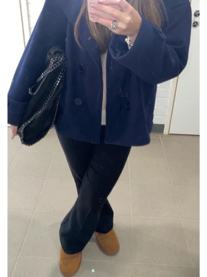 Mörkblå skepparkavaj med bred krage - Säljer en stilren mörkblå skepparkavaj med bred krage och dubbelknäppning framtill. Jackan har en loose passform och är tillverkad i ullmaterial som ger en lyxig och varm känsla. Perfekt för dig som gillar klassisk och cool stil.