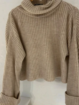 Beige ribbad polotröja - Mysig beige ribbad polotröja med bred krage och långa ärmar. Tröjan har en loose passform och är stickad i ett mjukt material som passar perfekt för kyliga dagar. Enkel att styla med jeans eller kjol för en avslappnad look.