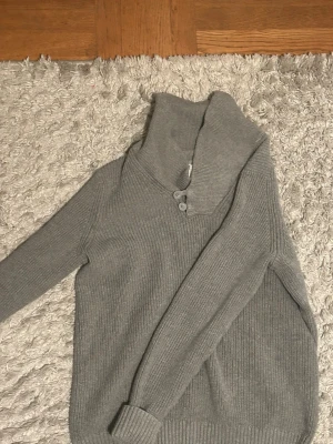 Grå stickad tröja Jean Pascale S - Säljer en grå stickad tröja från Jean Pascale i storlek S. Tröjan har hög krage med två knappar och ribbade muddar. Perfekt för kyliga dagar och enkel att matcha med jeans eller chinos.