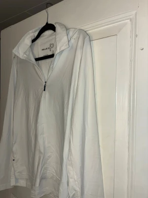 Vit långärmad tröja från Pelle P - Säljer en vit långärmad tröja från Pelle P med halv dragkedja framtill och hög krage. Tröjan har diskret logga på bröstet och bak i nacken. Tillverkad i ett lätt och mjukt syntetmaterial, perfekt för lager-på-lager under kyligare dagar.