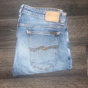 Nudie Jeans  - Snygga jeans från Nudie Jeans med klassisk femficksdesign och broderad bakficka. Midja 45cm, längd 109cm. Lagad på på knäna men det ser mest ut som coola slitningar och en söm är omsydd längst ned vid.benöppningen men det gör ingen skillnad. Nudie repair shop har gjort lagningarna så de är i grym kvalité. Modell skinny Sam. JAG SKICKAR EJ FLER BILDER NÄR JAG BÄR JEANSEN! för storleksguide hänvisar jag till måtten och för bättre inblick i passformen rekommenderar jag att googla på modellnamnet.26