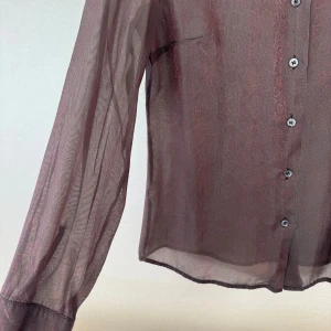 Brun blusskjorta från MAX&Co - Jättefin brun, skir blus/skjorta från MAX&Co med blommigt mönster som bara anas och diskret glans. Skjortan har klassisk krage, knappar framtill och är tillverkad i ett tunt, lätt material som ger en cool transparent effekt.