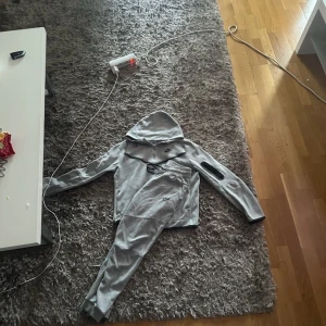 Grå Nike zip-hoodie XL - Säljer en grå Nike hoodie med dragkedja och huva. Jackan har svarta detaljer, Nike-logga på bröstet och en praktisk ficka på ärmen. Perfekt för chill dagar eller när du vill ha en sportig look. Mjuk och skön i bomullsmix.