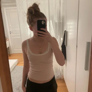 Ljusrosa ribbad linnetopp med spets - Supersöt ljusrosa ribbad linnetopp från H&M Divided med vit spets runt halsringningen och axelbanden. Modellen är ärmlös och har en slim passform. Materialet är mjuk bomull med lite stretch för extra komfort. Perfekt att styla med jeans eller kjol.