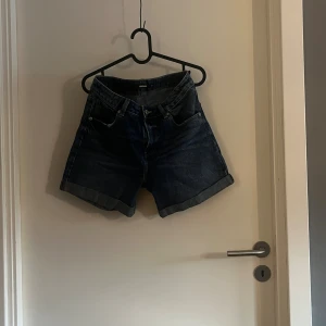 Mörkblå denimshorts från Bik Bok - Snygga mörkblå jeansshorts från Bik Bok i klassisk femficksmodell. De har hög midja, breda uppvikta benslut och tydliga sömmar. Passar dig som vill ha lite längre shorts.