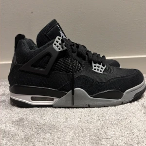Nike Air Jordan 4 Retro svart/grå - Nike Air Jordan 4 Retro sneakers i svart och grått med röda detaljer på yttersulan. Skorna har meshpaneler, snörning och ikoniska Jumpman-loggor på hälen. Ovandelen är i syntet och mocka, med platt sula och rund tå. Perfekt för dig som gillar streetwear och klassiska sneakers.