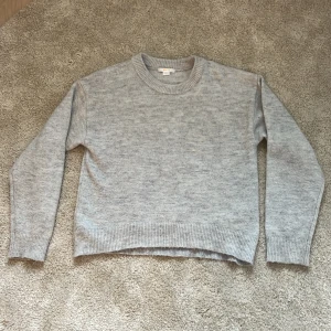 Grå tröja från Gina tricot  - Grå stickad tröja från ginatricot i storlek 158-164. Tröjan sitter ganska avslappnat och har ett mjukt material. Köptes för drygt 1 år sen men har bara använts ett fåtal gånger. Det finns ett litet hål vid den vänstra armen fast det går att sy igen