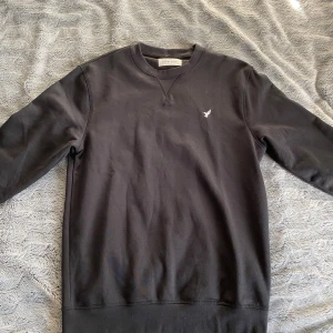 Svart och grå sweatshirt från Pier One - Två stilrena sweatshirts från Pier One, en i svart och en i grått. Båda har rund halsringning, lång ärm och en liten broderad fågel på bröstet. Tillverkade i mjuk bomullsmix som är skön mot huden och passar perfekt till jeans eller joggers. Skick 9,5/10 (150 kr för båda)