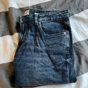 Mörkblå jeansbyxor från Pull&Bear - Säljer ett par mörkblå jeansbyxor från Pull&Bear med klassisk femficksdesign och snygg tvätt. Jeansen har normal passform och raka ben, perfekta för en avslappnad stil. Materialet är slitstarkt denim i bomull.