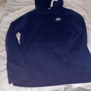 Mörkblå Nike hoodie med huva - Säljer en mörkblå hoodie från Nike med klassisk logga på bröstet. Tröjan har huva, lång ärm och en stor magficka framtill. Perfekt för en avslappnad och sportig stil.