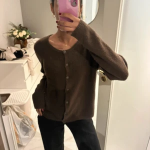 Brun stickad kofta med knappar - Mysig brun stickad kofta med rund halsringning och knäppning framtill. Koftan har långa ärmar och en relaxed passform, perfekt att slänga på sig när det är kyligt. Enkel och stilren design som funkar till många outfits.