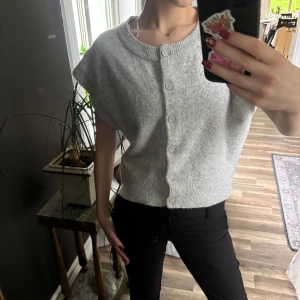 Grå ärmlös kofta med knappar - Superfin ljusgrå kofta med korta ärmar och knäppning framtill. Den är stickad och har en bred ribbad kant vid halsen💕 
