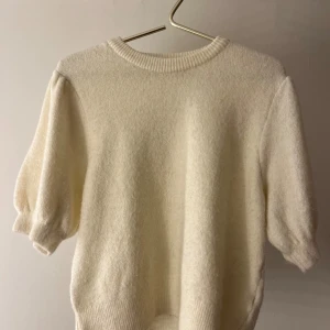 Vit stickad tröja från Gina Tricot - Superfin vit stickad tröja från Gina Tricot med korta puffärmar och rund halsringning. Tröjan har ribbade muddar vid ärmslut och nederkant, vilket ger en snygg och modern look. Perfekt för lager-på-lager under hösten och vintern.