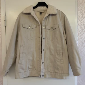 Beige teddyjacka med fuskpälsfoder - Nypris: 400kr. Endast använd ett par gånger. Jackan har klassisk jeansjacke-look med bröstfickor med knappar, sidofickor och silverfärgade detaljer. Perfekt för dig som vill ha en chill och varm stil under höst och vinter.