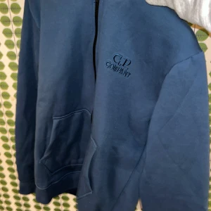 Blå hoodie med goggles från C.P. Company - Säljer en blå hoodie från C.P. Company med deras ikoniska goggles i huvan. Tröjan är aldrig använd och inte ens plasten på glasögonen är avdragna. Cp company påse kommer med, samt tagsen.