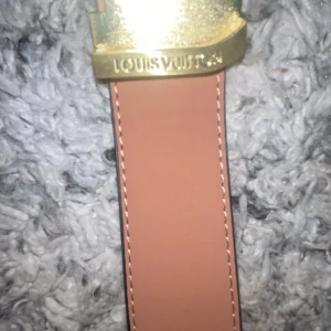 Beige Louis Vuitton skärp med gulddetalj - Säljer ett stilrent beige Louis Vuitton bälte med exklusivt guldfärgat spänne där loggan är ingraverad. Bältet är tillverkat i slätt skinn och har ljusa sömmar längs kanterna. Kommer med original ask, dustbag och påse från Louis Vuitton.