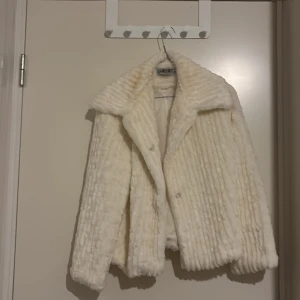 Vit pälsjacka från Khawam - Säljer en fluffig och lyxig vit pälsjacka från Khawam. Jackan har bred krage, markerad struktur och är helfodrad med satinliknande tyg på insidan. Perfekt för dig som vill sticka ut och hålla dig varm med stil.