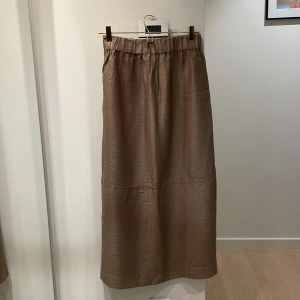 Glittrig brun långkjol | Levete Room - Säljer en snygg brun långkjol från Levete Room i storlek S. Kjolen har glittrig finish, resår i midjan och en rak, avslappnad passform. Endast använd ett förtal gånger :) 