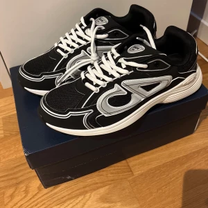 Dior b30 - Snygga Dior-sneakers i svartvitt med framträdande 'CD'-märkning på sidorna. Levereras med originalkartong.                               ⭐️ Skick: 10/10 🎲 Storlek: 43 🎨 Färg: Svart och Vit 📦 Snabb och trygg frakt.   Pris kan diskuteras