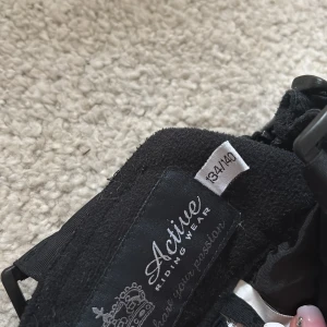 Svarta täckbyxor från Active Riding Wear - Svarta täckbyxor från Active Riding Wear med förstärkta partier på insidan av benen och sätet, justerbara hängslen och reflexdetaljer vid bensluten. Perfekta för ridning under kalla dagar, med slitstarka material och praktiska fickor.