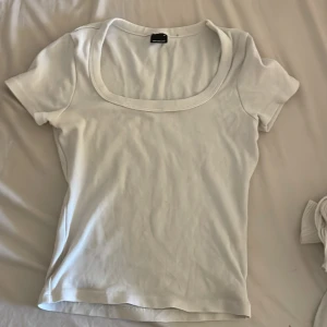 Vit ribbad topp från Gina Tricot - Säljer en vit ribbad topp från Gina Tricot i storlek M. Toppen har en bred, rundad halsringning och korta ärmar. Materialet är mjukt och stretchigt, vilket gör den skön att bära. Perfekt att styla med jeans eller kjol för en clean look.