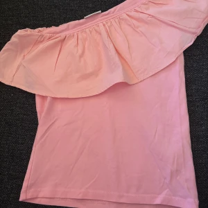 oneshoulder topp  med volang - Säljer min söta topp. Knappast använd. Skriv privat för fler bilder. Pris kan diskuteras!💗Är storlek 158/164 men passar som XS.