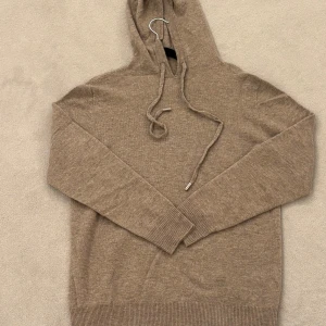 Beige stickad hoodie med huva - Säljer en beige stickad hoodie med huva och snörning. Tröjan har långa ärmar och ribbade muddar vid ärmslut och nederkant. Perfekt för dig som gillar en chill och avslappnad stil. Helt ny. Finns i fler färger 