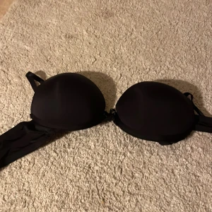 Svart bh med vadderade kupor - Snygg svart bh med vadderade kupor och justerbara axelband. Klassisk och stilren modell som ger bra stöd. Perfekt för strandhäng eller poolparty. Materialet känns mjukt och följsamt mot huden. Bygeln har åkt ut lite 