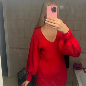 Röd stickad klänning med v-ringning - Säljer en snygg röd stickad klänning med v-ringad hals och långa, puffiga ärmar. Klänningen är ribbad och har en kroppsnära passform som framhäver figuren. Endast använd en gång så i ny skick. Jag är 183cm och den går strax under knäna☺️