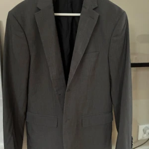 Mörkgrå kavaj HM stl 52 Ny - MörkGrå kavaj med en slim fit passform från H&M. Kavajen har två knappar fram och en bröstficka. Stl 52. Ny.