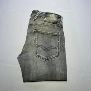 Replay grå jeans, W28 L32 - Snygga grå jeans från Replay. Jeansen har raka ben, normal passform  och coola detaljer på bakfickorna. Perfekta för dig som gillar en avslappnad men stilren look. Jeansen har en liten slitning i skrevet som man kan se på den  andra bilden. 
