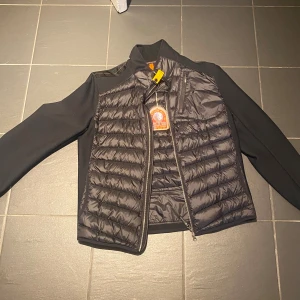 Svart pufferjacka från Parajumpers - Snygg svart pufferjacka från Parajumpers med quiltad framsida och släta ärmar. Jackan har dragkedja framtill, hög krage och en gul detalj vid halsen. Perfekt för dig som vill ha en stilren och sportig look, den är helt ny inte använd någon gång.
